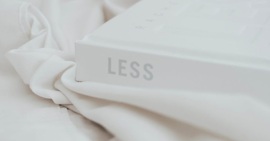 A minimalist still life featuring a book with 'LESS' on the cover and a terracotta mug.